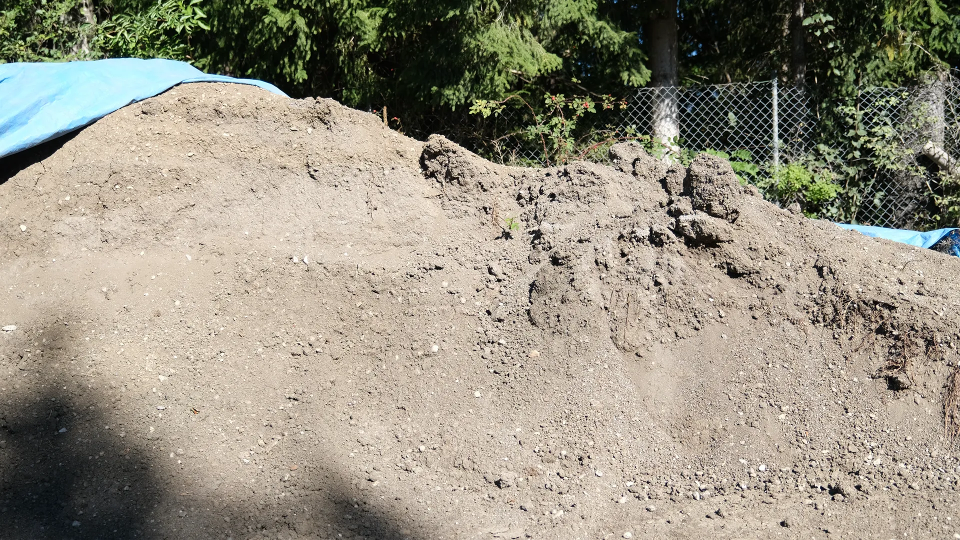 Hoher Haufen aus hellbrauner Erde vor einem Zaun