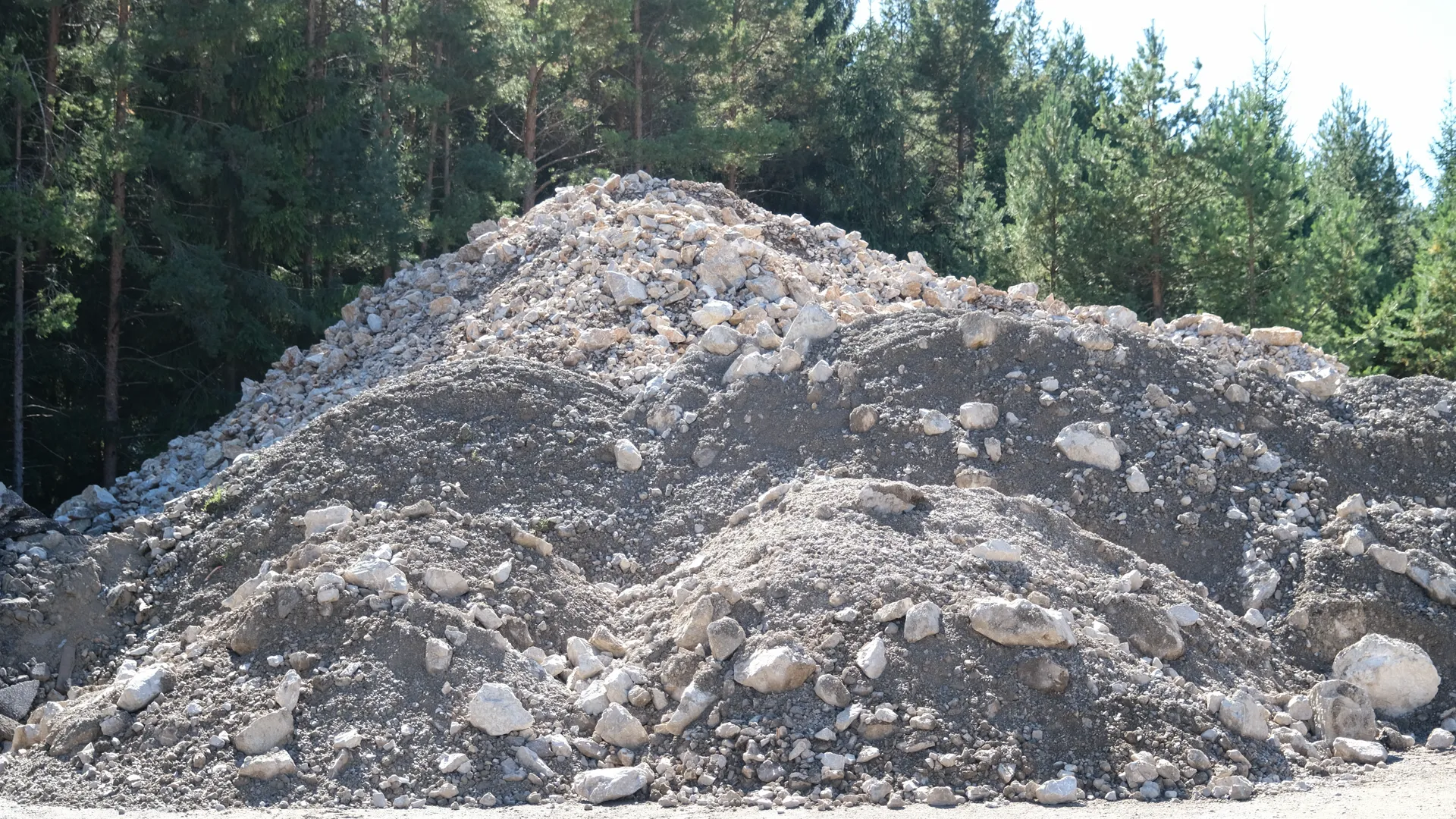 Haufen aus grauem Bruchmaterial mit Steinen vor Nadelwald